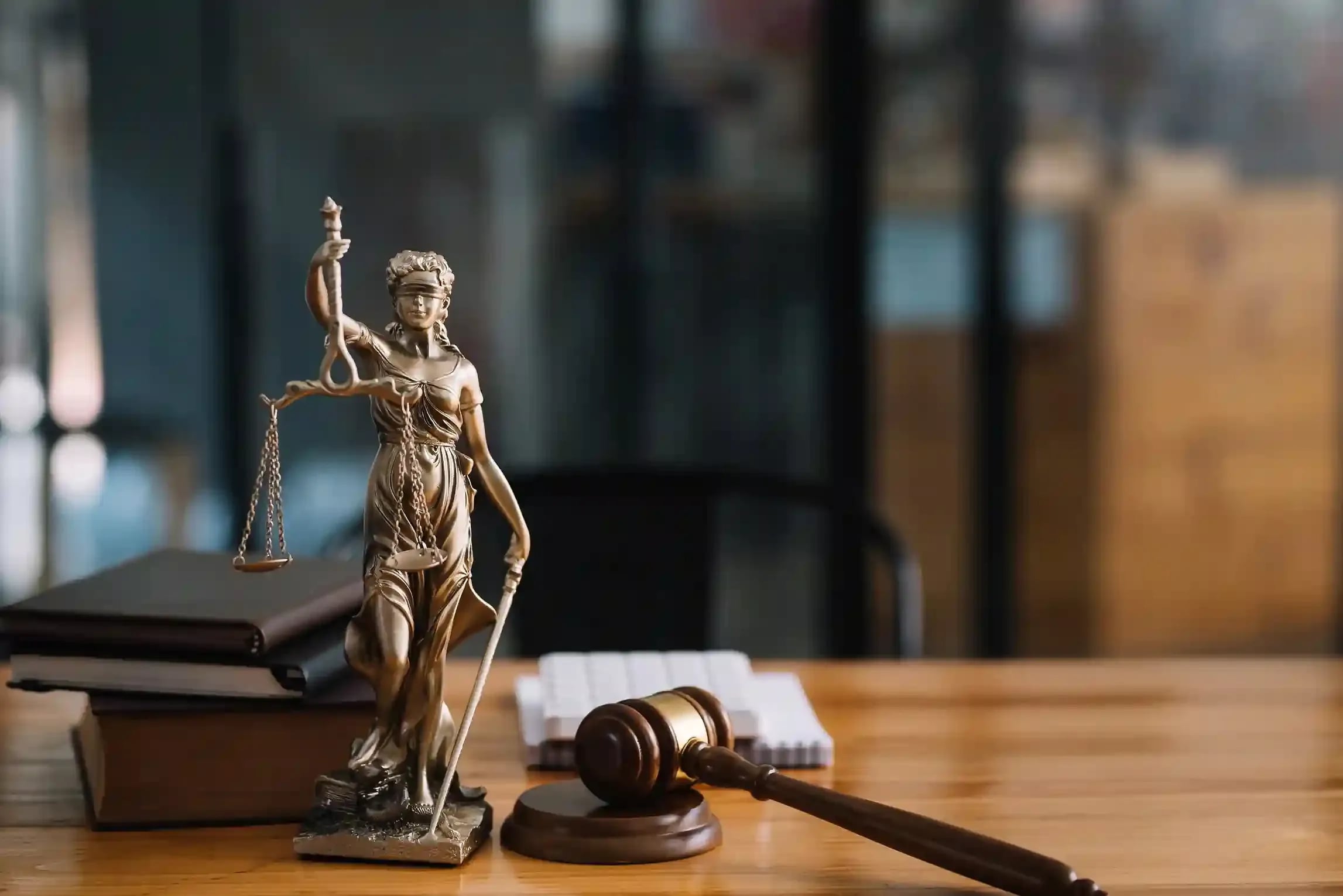 Justitia und Richterhammer auf einem Schreibtisch.